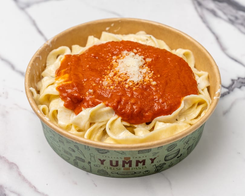 Yummy Cheese Pasta with fettuccine, red sauce, and grated cheese in a branded takeout container.
