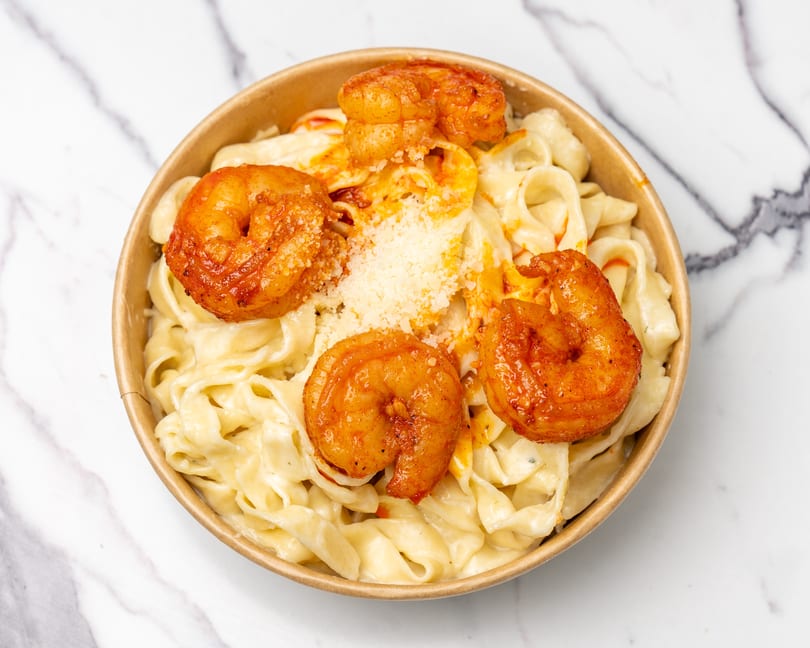 Creamy fettuccine alfredo with five large, seasoned shrimp and grated cheese in a bowl.