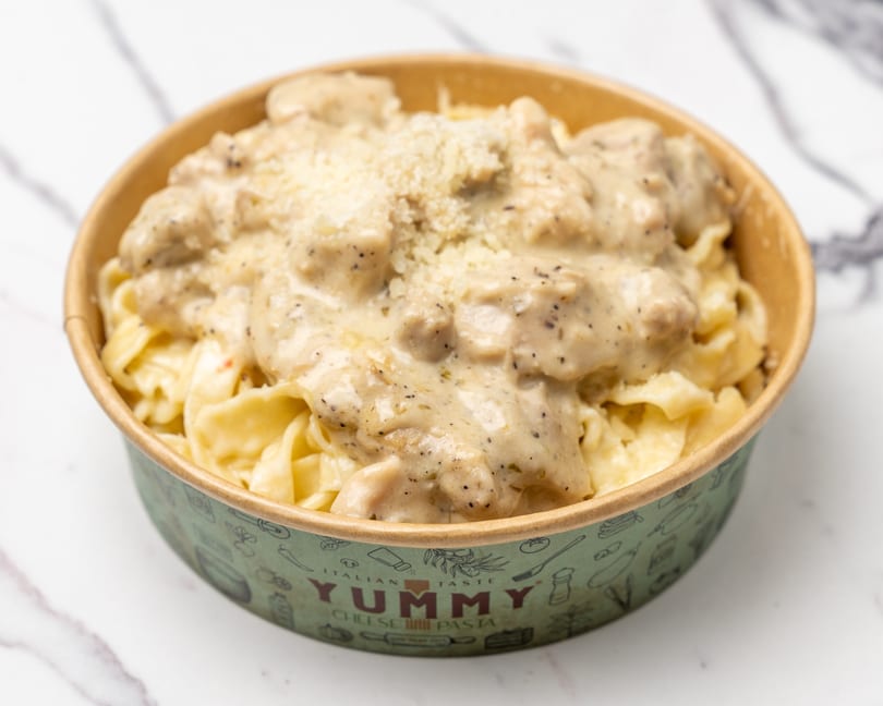 Creamy chicken pasta with grated cheese in a Yummy Cheese Pasta branded bowl.