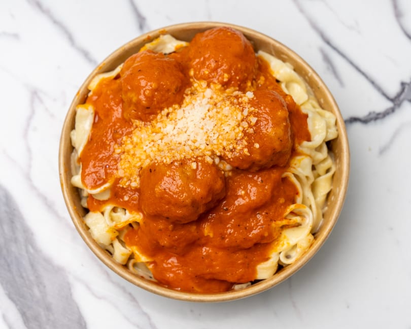 Pasta with meatballs and red sauce, topped with grated cheese in a brown bowl.