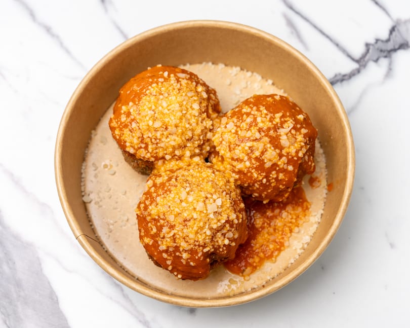 Three meatballs covered in red sauce and grated cheese, served in a brown bowl.