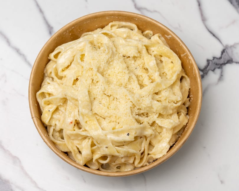 Creamy fettuccine alfredo pasta topped with grated parmesan cheese in a brown bowl.