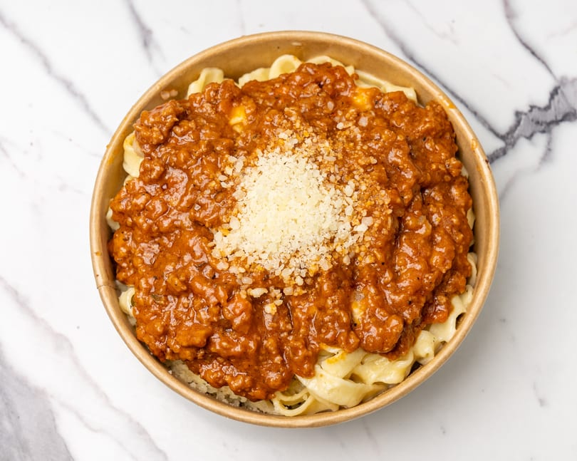 Pasta with a rich red meat sauce and a sprinkle of grated cheese in a round bowl.