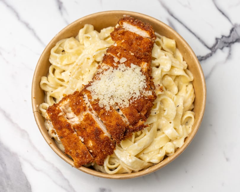 Crispy breaded chicken cutlets with grated cheese on a bed of creamy fettuccine pasta in a bowl.